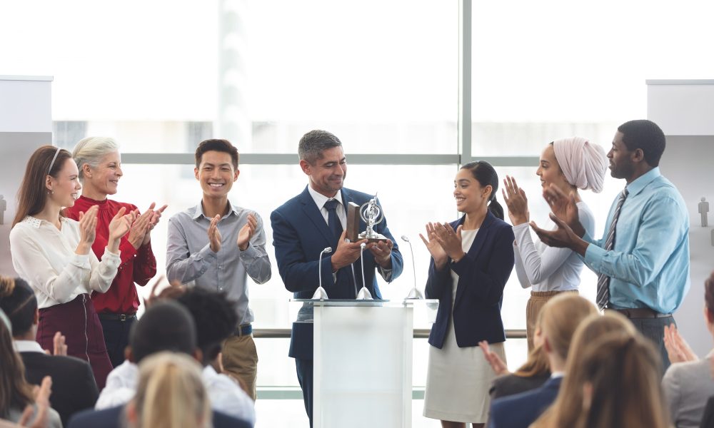 businessman-holding-award-on-podium-with-colleagues-at-business-seminar.jpg